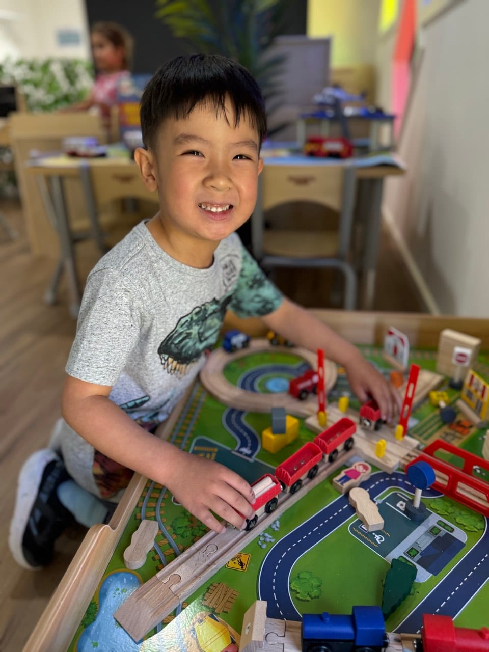 A child smiling while building and arranging play materials indoors.