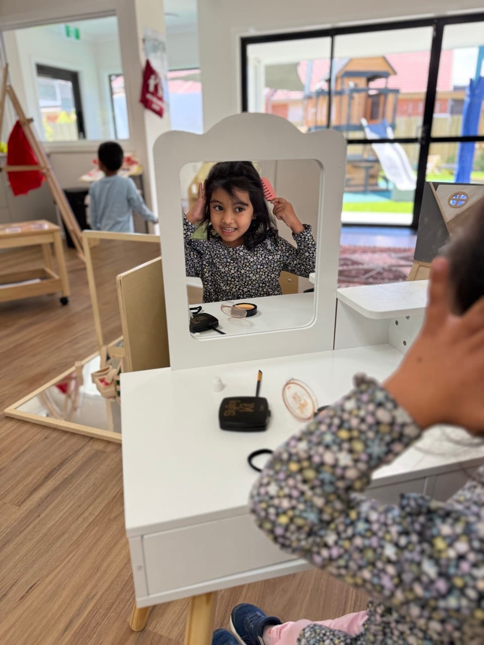 A child exploring a mirror and vanity play space during indoor learning time.