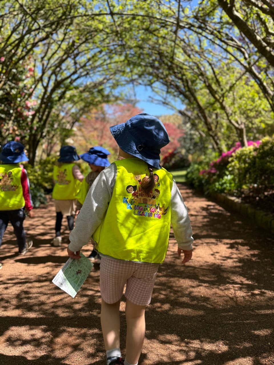 A child in a high-visibility vest walking along a shaded nature path.