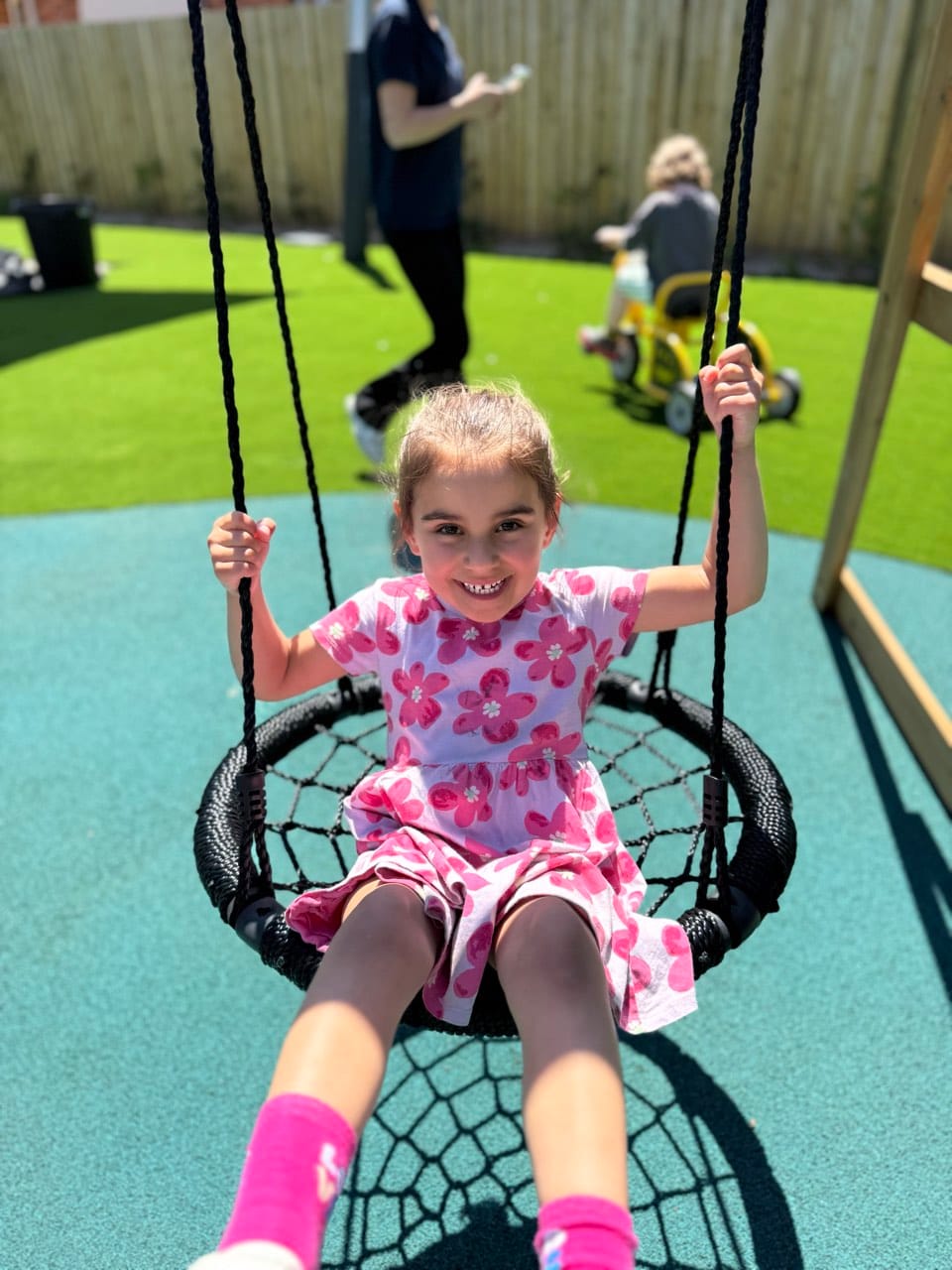 A child enjoying a nest swing during outdoor play at Kids Kingdom.