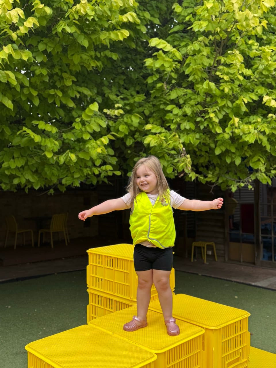A child standing confidently on a yellow play platform outdoors.